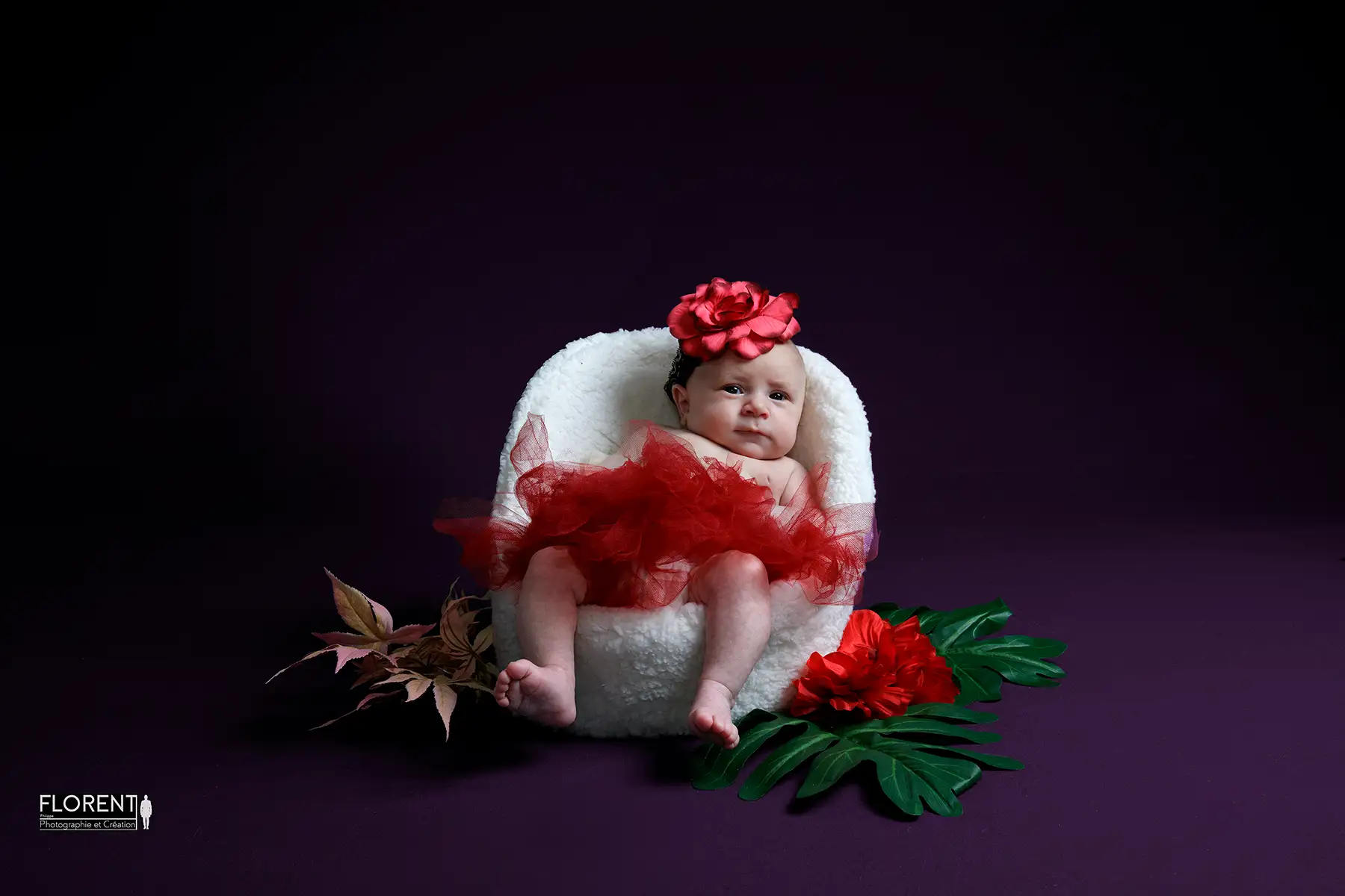 photo bébé avec fleurs rouges nous regarde souriante dans petit fauteuil fanie photographe florent studio boulogne sur mer lille le touquet paris calais saint omer berck